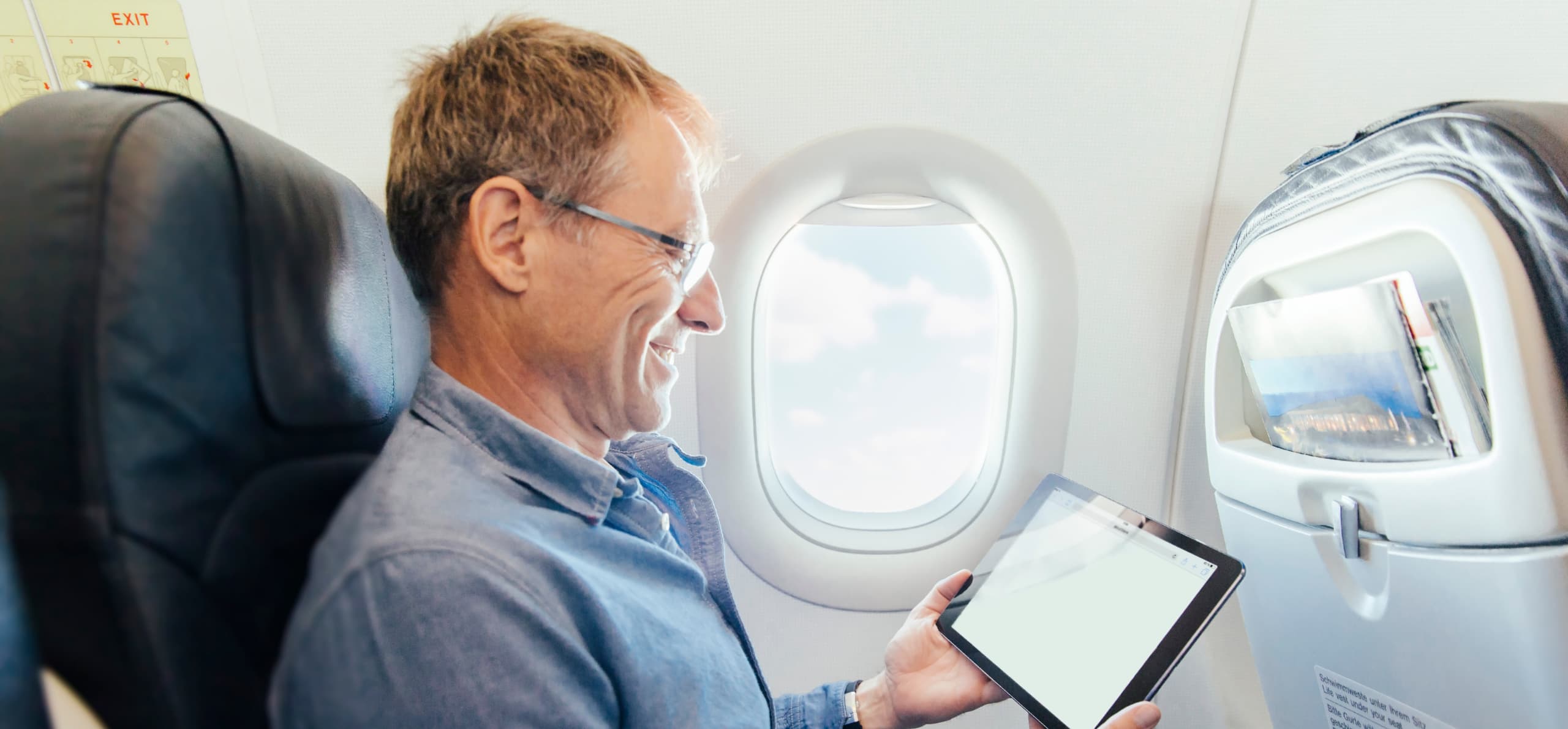 Man seated on an airplane viewing a tablet